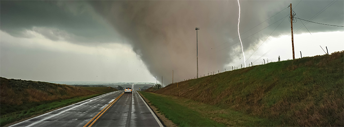 Image of a massive tornado and lightning strike along a rural road with only 1 car on it.